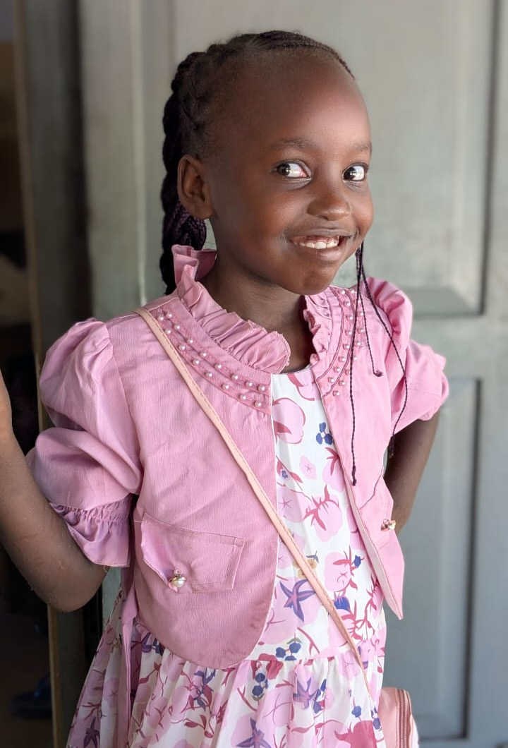 Una bambina con un vestito rosa sorride sulla porta